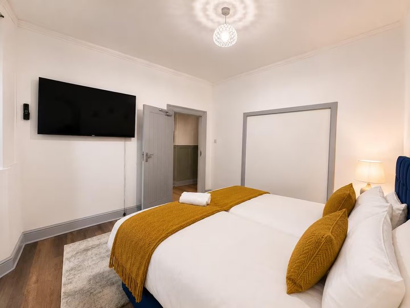 Modern bedroom with double bed, gold bedding, wall-mounted TV, and ensuite door