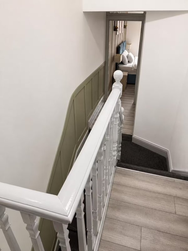 Staircase landing with white bannister and green panelled wall, wooden flooring visible