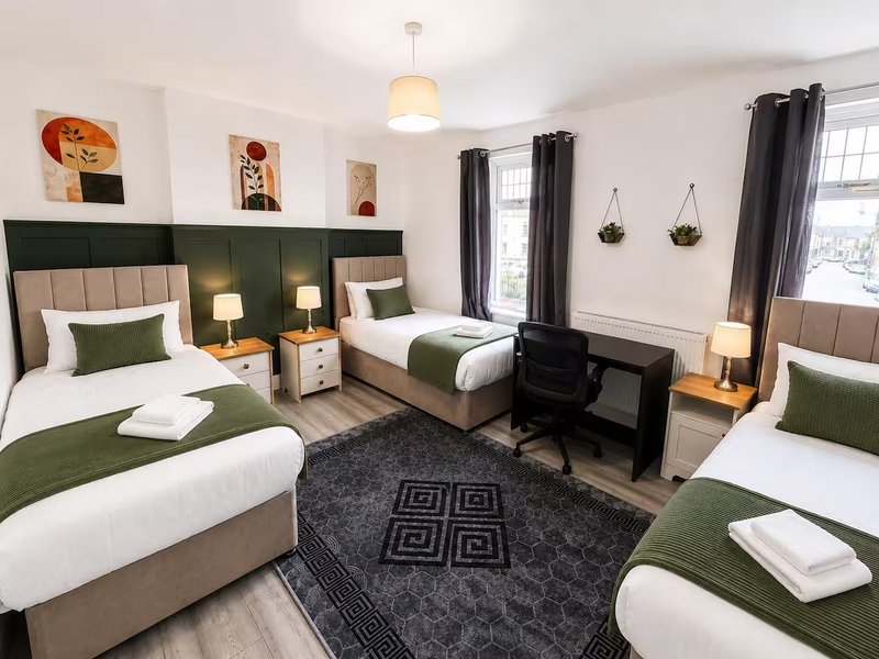 Spacious bedroom with three beds, green headboards, and modern furnishings throughout