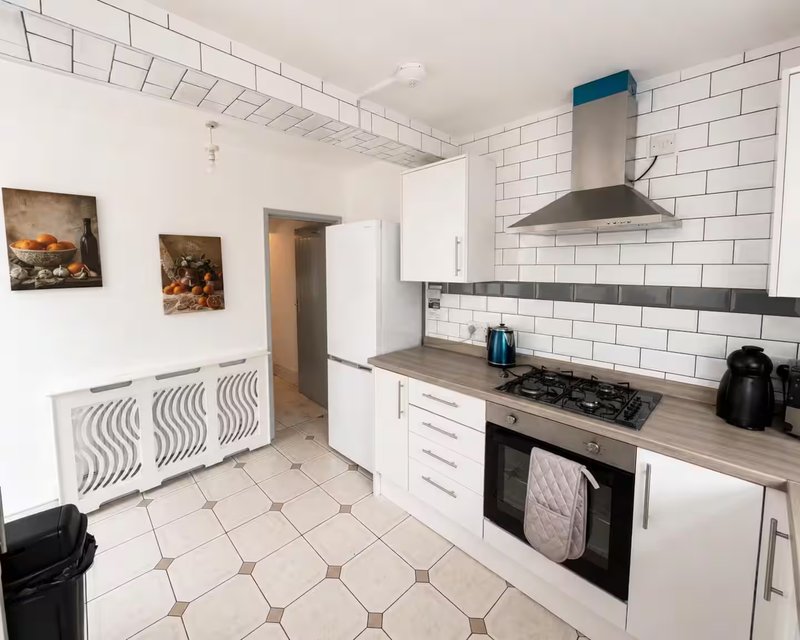 Modern kitchen with white cabinetry, subway tile backsplash, stainless steel cooker hood and gas hob
