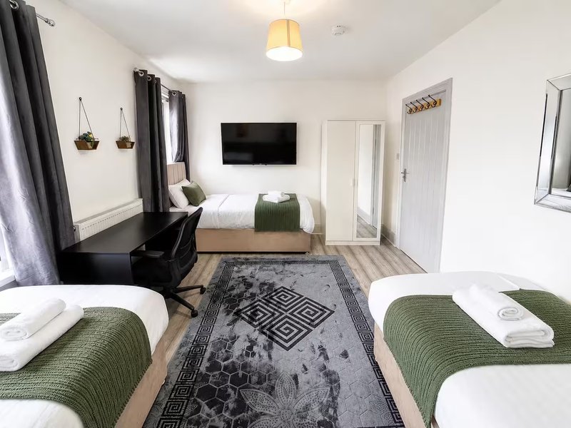 Modern bedroom with three beds, desk, TV, and geometric patterned rug