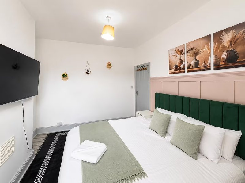 Modern bedroom with double bed, green headboard, white bedding, and wall-mounted TV