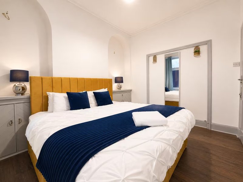 Modern bedroom with mustard-yellow upholstered bed, navy bedding, white pillows and wooden floor