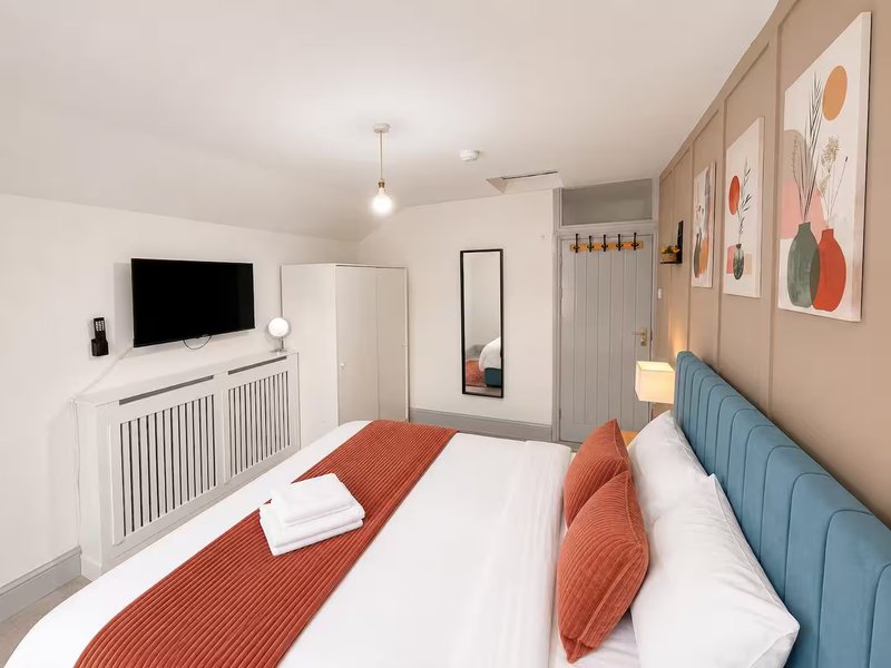 Modern bedroom with double bed, blue headboard, white bedding, TV on wall, and decorative wall art