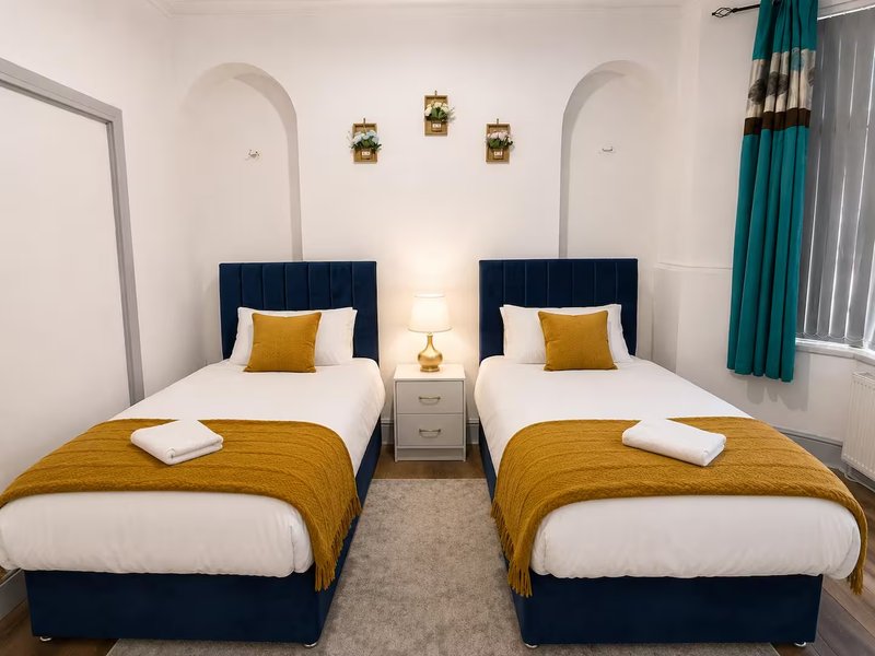 Twin bedroom with two single beds, navy headboards, gold throws, and teal curtains