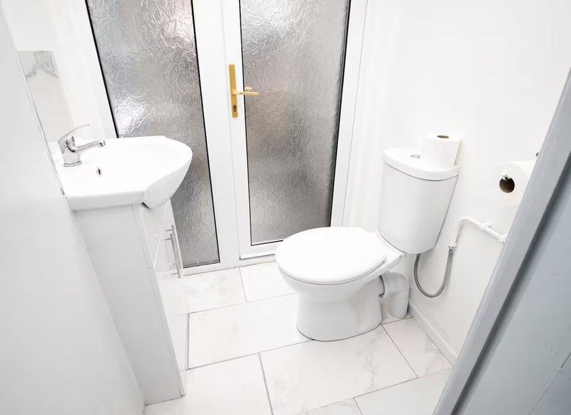Clean white bathroom with toilet, sink, shower cubicle and tiled floor