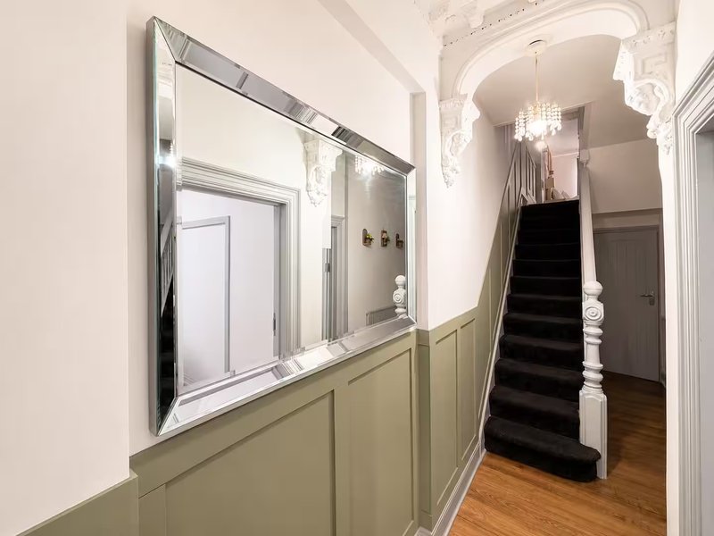 Elegant hallway with large mirror, wainscoting, staircase with chandelier overhead