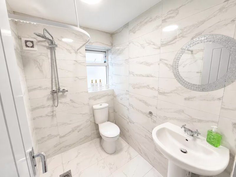 Modern bathroom with marble tiles, walk-in shower, toilet, sink and decorative mirror