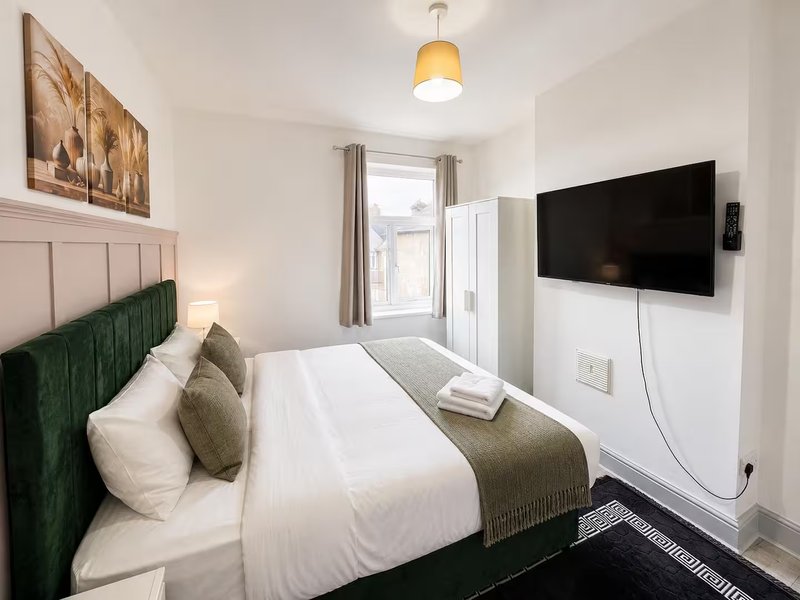 Modern bedroom with green upholstered bed, white bedding, wall-mounted TV and door to balcony