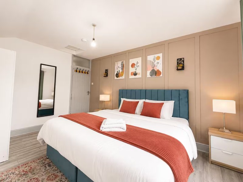 Modern bedroom with teal upholstered bed, white linens, red throw, framed wall art, and bedside lamps
