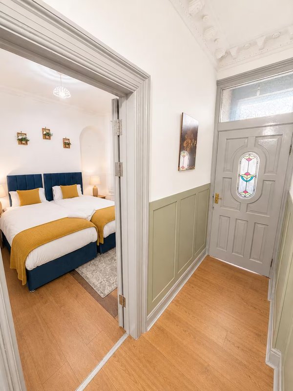 Bedroom hallway with wooden floor, white walls, and open doorway to bedroom with blue and gold bedding