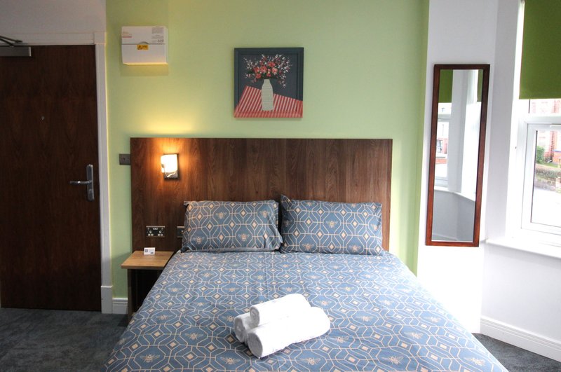 Bedroom with double bed, patterned blue bedding, wooden headboard, green walls, bedside lamp