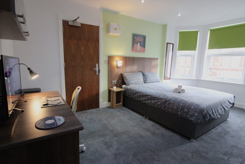 Bright bedroom with double bed, desk, wooden door and green window blinds
