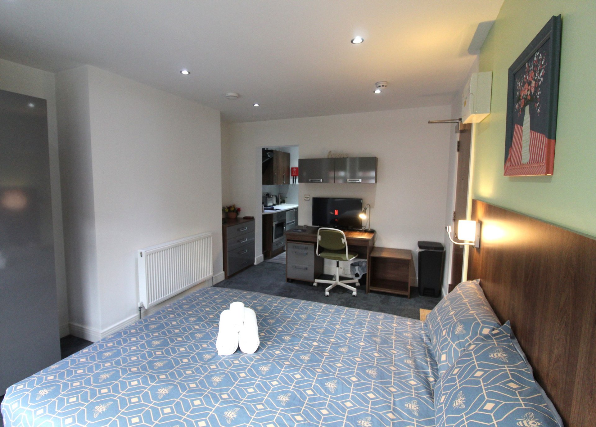Spacious bedroom with double bed, desk area, shelving, and green accent wall