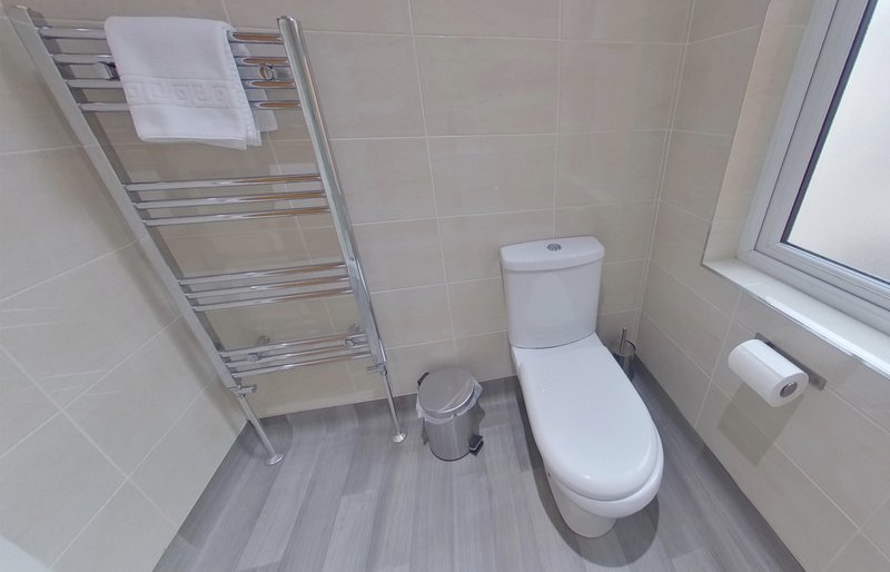 Small bathroom with toilet, heated towel rail, window and tiled walls