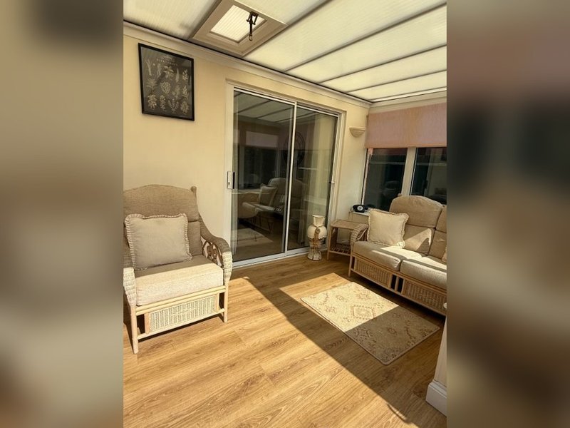 Bright conservatory with wooden flooring, wicker armchair, sofa, and glass sliding doors