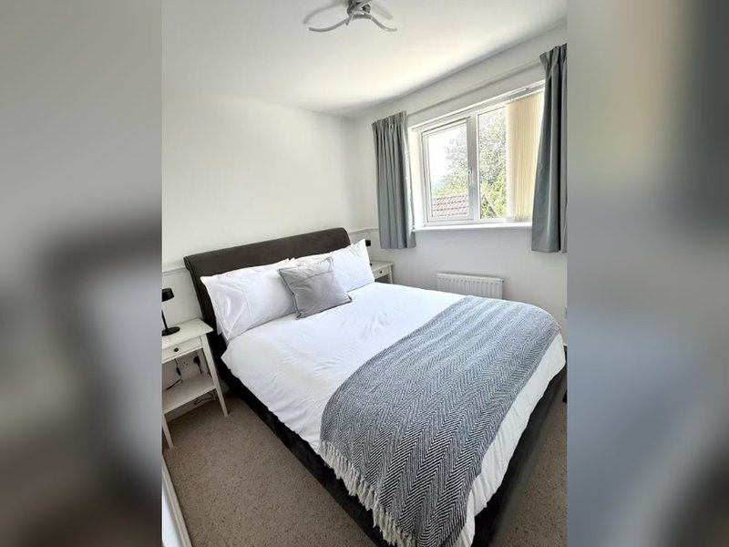 Bright bedroom with double bed, grey bedding, white pillows and window with curtains
