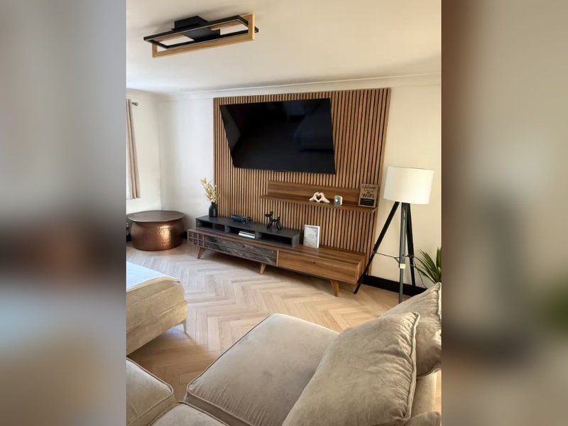 Modern living room with wall-mounted TV, wooden media console, sofa with cushions, and herringbone flooring