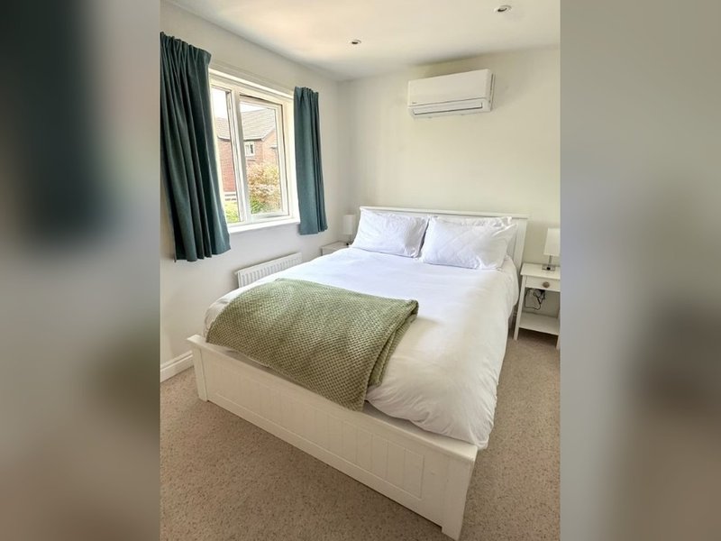 Bright bedroom with double bed, white bedding, green throw blanket, window with dark curtains
