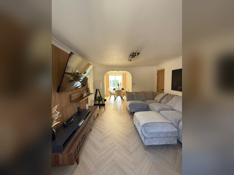 Modern open-plan living room with grey sectional sofa, wooden TV unit, and herringbone flooring