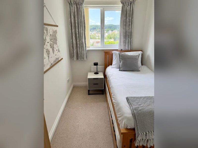 Compact bedroom with single bed, window with countryside view, bedside table and grey curtains
