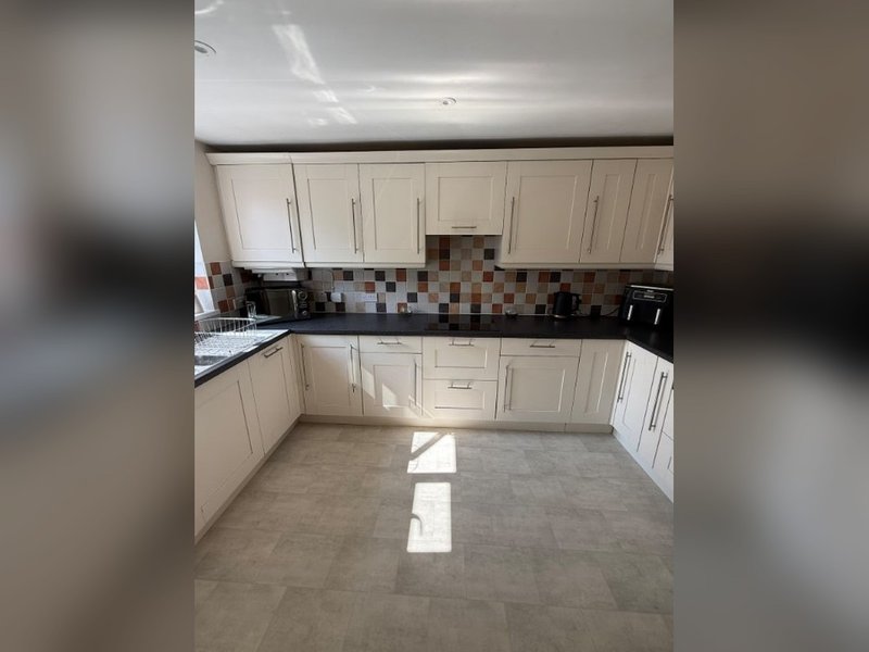 Modern kitchen with white cabinetry, tiled backsplash, black countertops and beige flooring