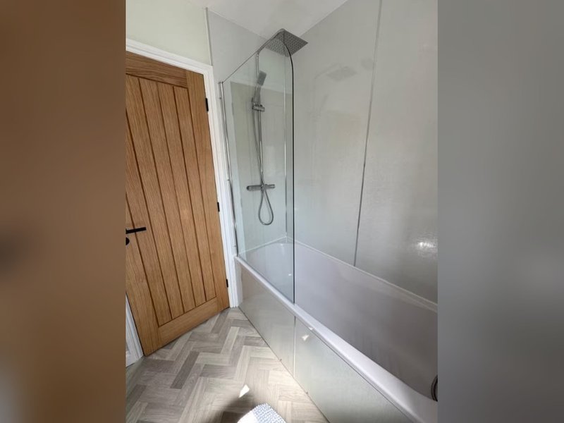 Modern bathroom with walk-in shower enclosure, wooden door and chevron tile flooring