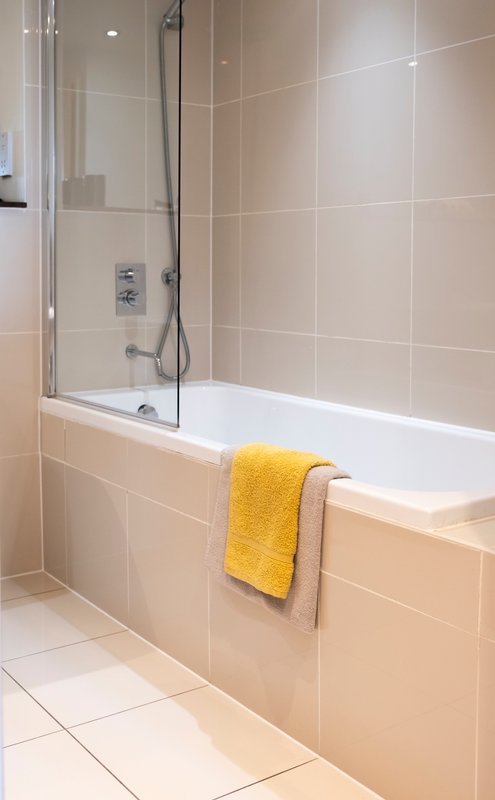 Modern bathroom with white bathtub, glass shower screen, yellow towel rail, and beige wall tiles