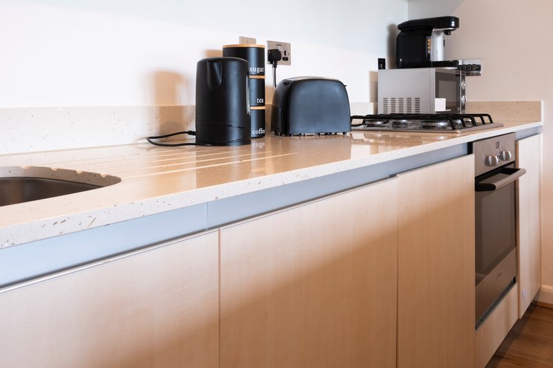 Modern kitchen with white cabinetry, wooden countertop, black kettle and coffee maker