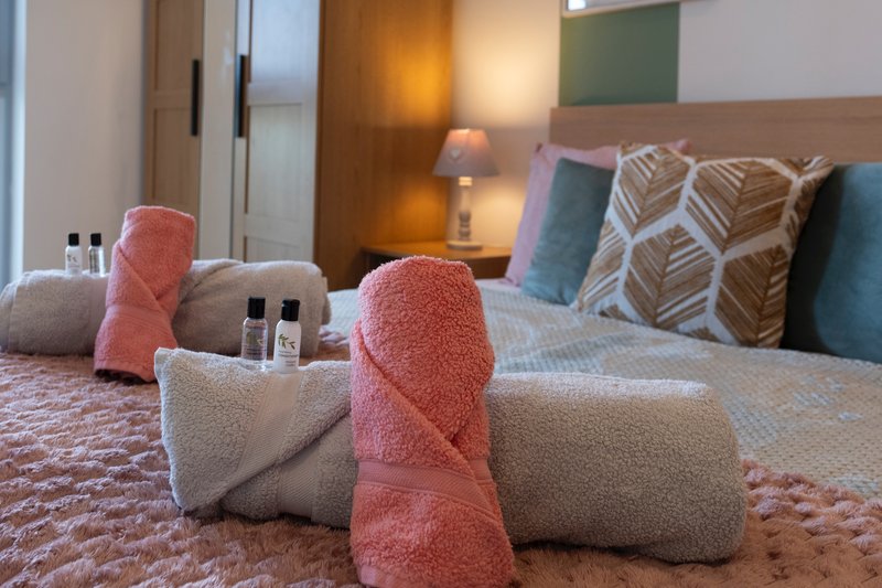 Hotel bedroom with rolled towels, toiletries, pillows and bedside lamps