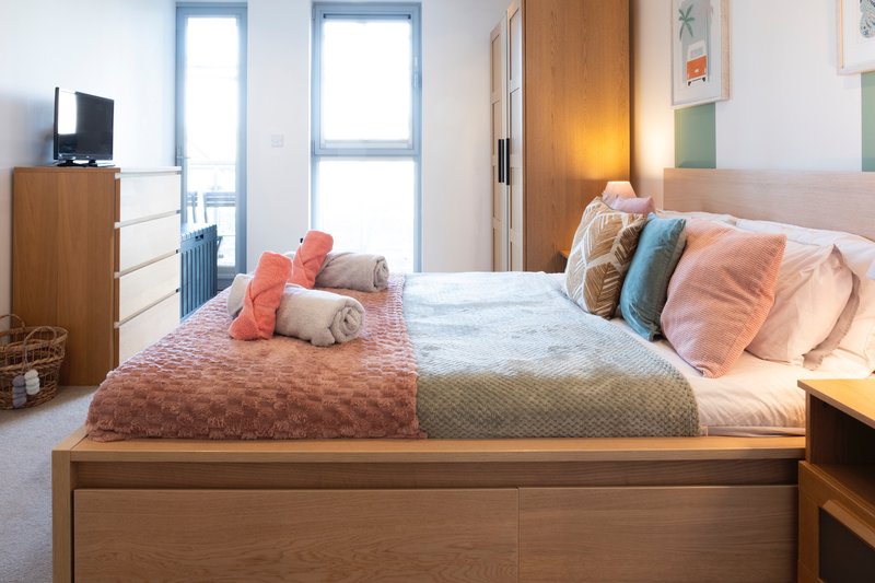 Bright bedroom with double bed, wooden furniture, colorful cushions and pillows