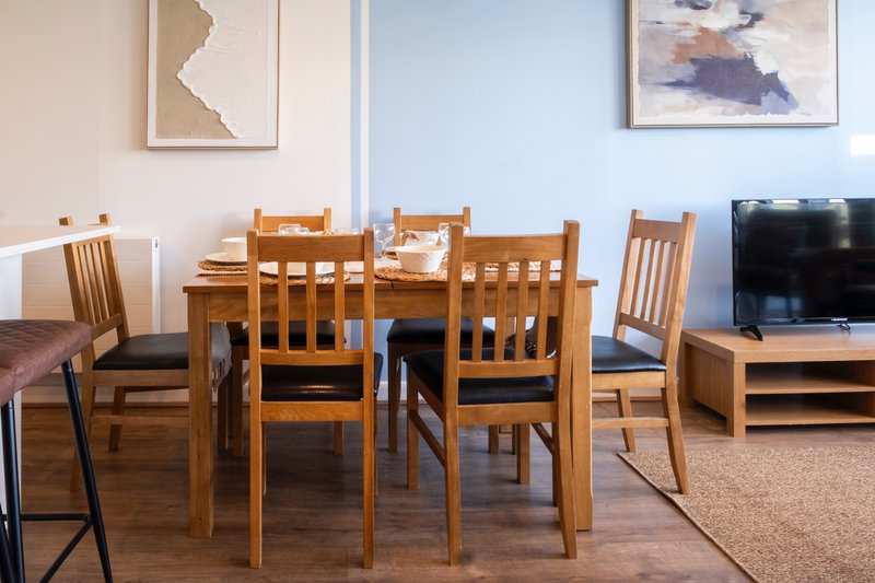 Open-plan living and dining area with wooden dining table, chairs, TV, and framed wall art