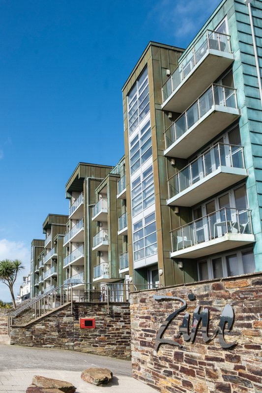 Modern multi-story apartment building with balconies, stone base wall, and clear blue sky