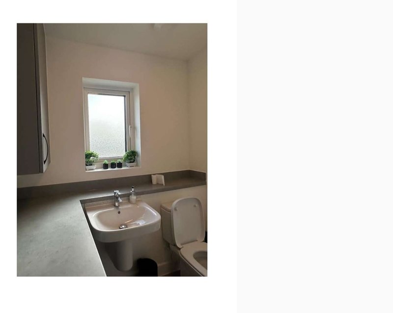 Bathroom with pedestal sink, window, toilet, and beige tiled walls