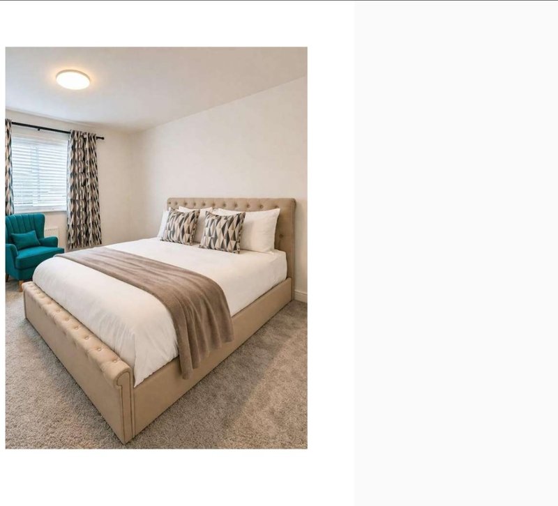 Bright bedroom with upholstered bed, white bedding, patterned cushions, and teal armchair by window