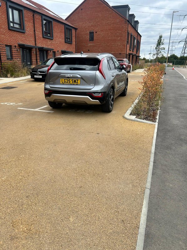 Brick residential building with parking area, parked silver car and landscaped grounds