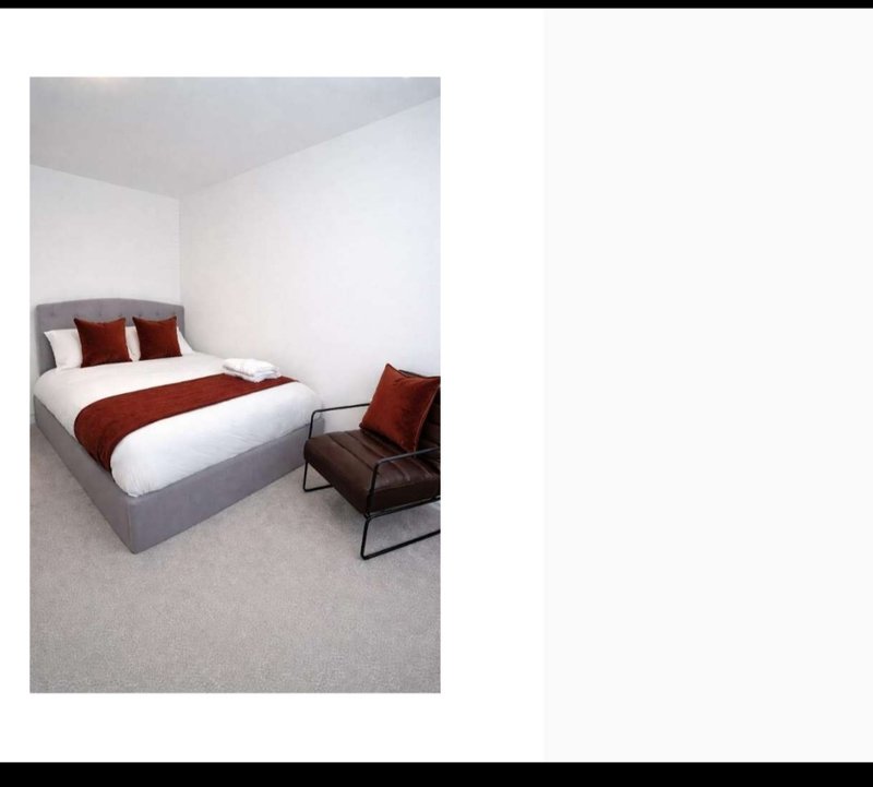 Modern bedroom with double bed, red bedding, white pillows, and leather accent chair