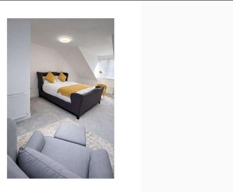 Attic bedroom with double bed, yellow bedding, grey armchair and ceiling light