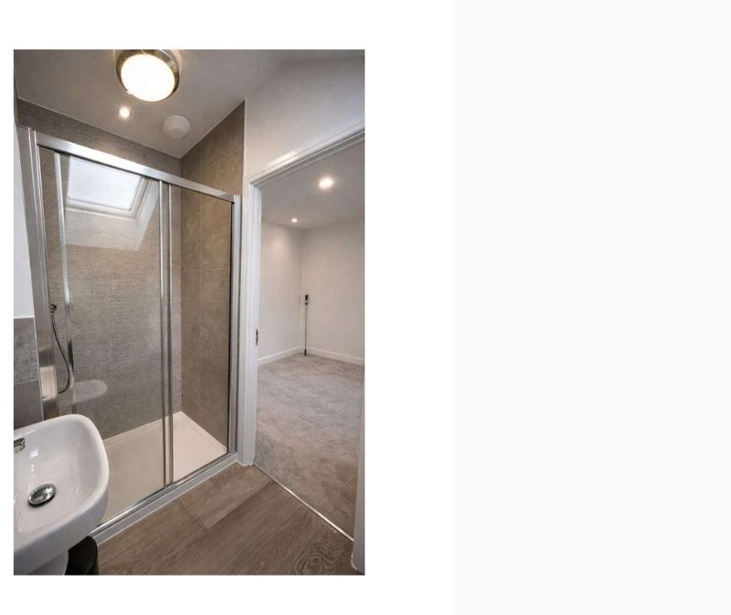 Modern bathroom with walk-in shower enclosure, white sink, and wooden floor