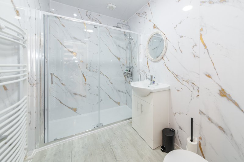 Modern bathroom with marble-effect tiled walls, walk-in shower enclosure, white vanity sink and mirror