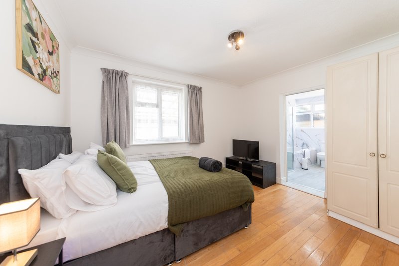 Bright bedroom with double bed, olive green bedding, wooden floor, and white fitted wardrobes