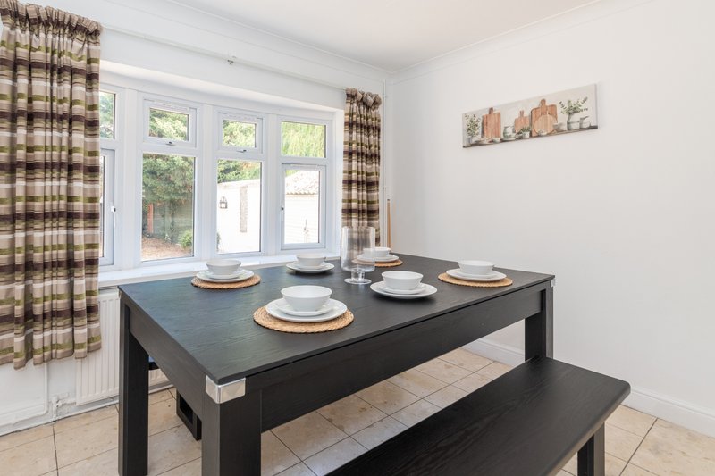Dining area with black table, place settings, bench seating, and large windows overlooking garden