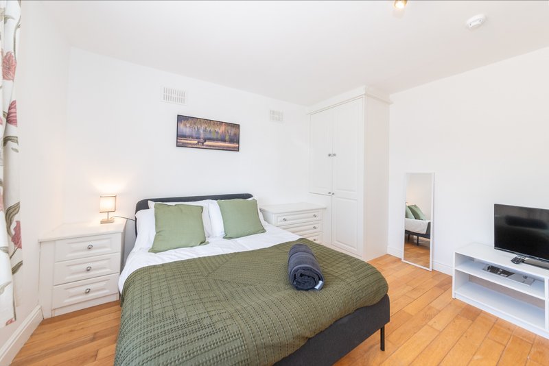 Bedroom with double bed, green bedding, wooden floor, white storage and TV