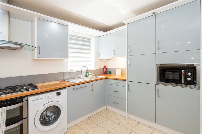 Modern kitchen with light blue cabinetry, wooden countertop, integrated appliances and washing machine