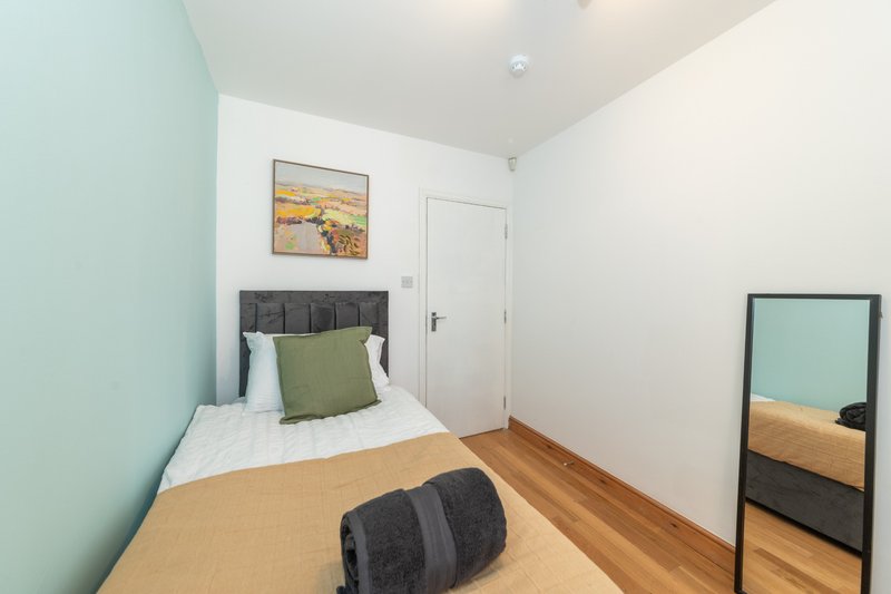 Compact bedroom with single bed, green accent wall, wooden floor and mirror