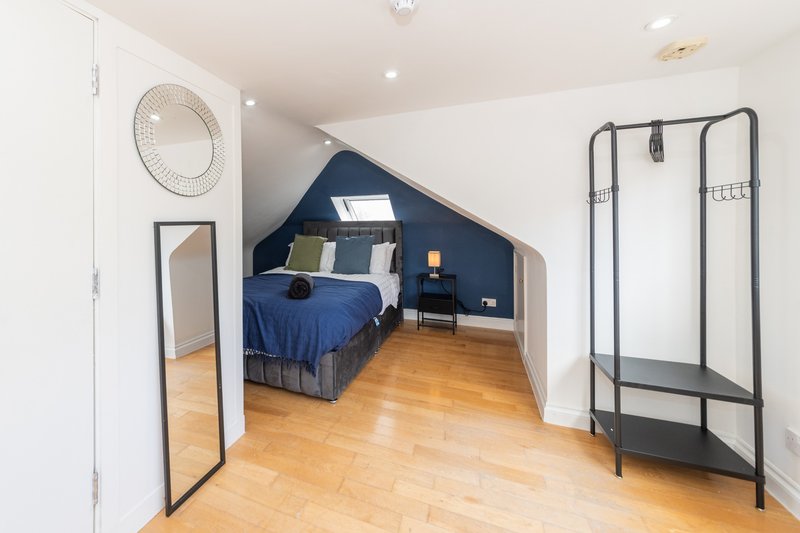 Attic bedroom with navy blue bed, wooden floor, clothing rack and round mirror