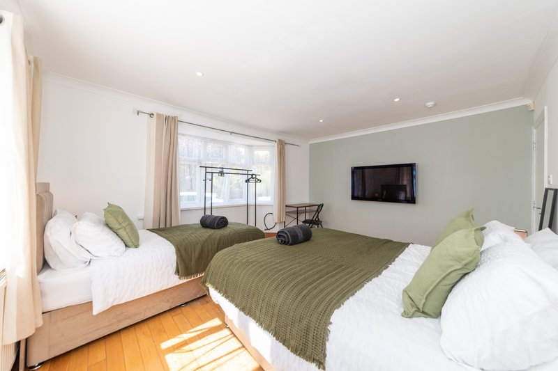 Bright bedroom with three beds, green bedding, wooden floors and wall-mounted TV