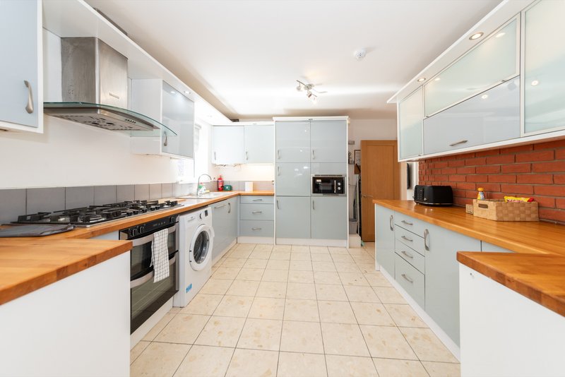 Modern kitchen with white cabinetry, wooden countertops, stainless steel appliances and red brick splashback