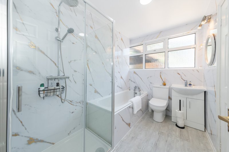 Modern bathroom with marble-effect shower enclosure, white vanity, toilet and bright windows
