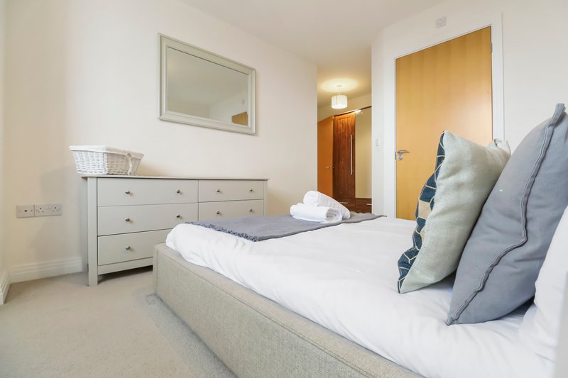 Bedroom with double bed, white bedding, blue and grey pillows, wooden dresser and mirror